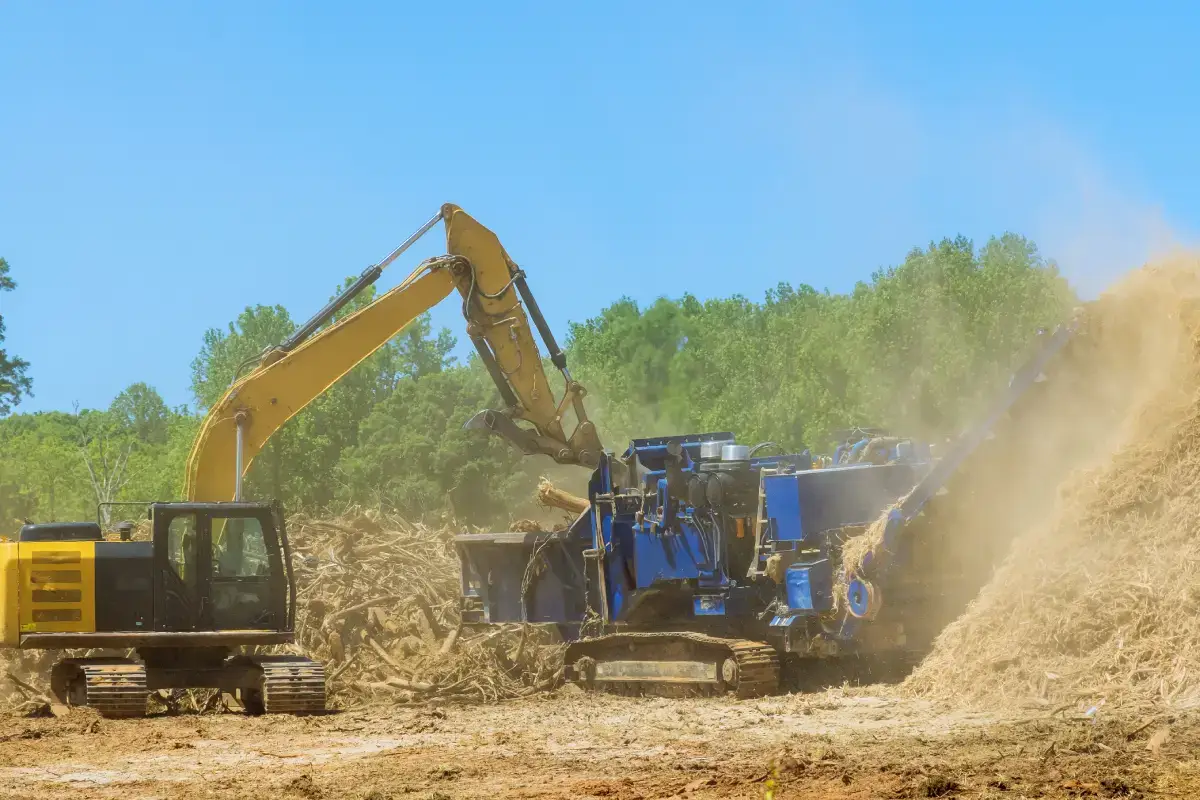 Excavator feeding land clearing debris into a tub grinder