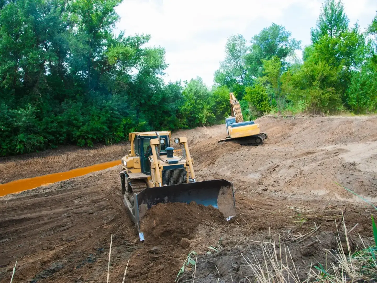 Bulldozer and excavator grading a pond embankment